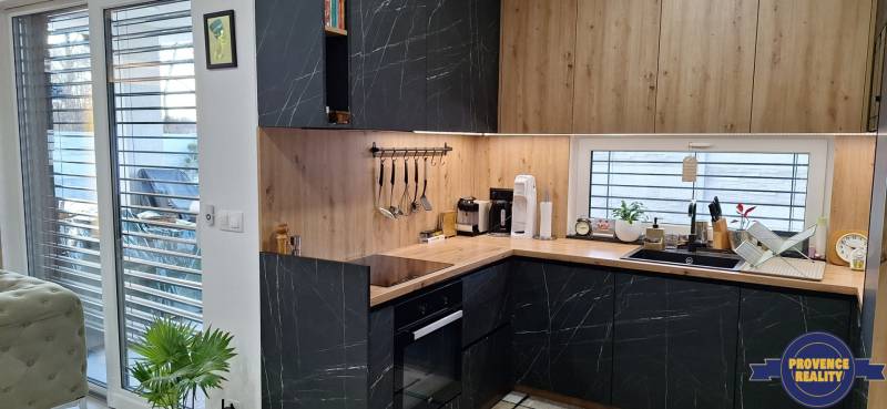 Kuchyňa v rodinnom dome s tmavými skrinkami a dreveným dekorom, svetlá cez veľké okná.