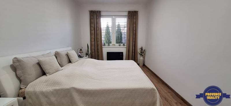 Spálňa v rodinnom dome s posteľou, závesmi a podlahou s dreveným dekorom.