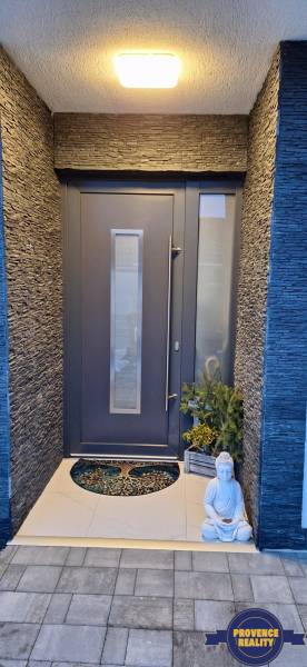 Exteriér rodinného domu v Kolárove s modernými dvermi, so sochou a rastlinou.