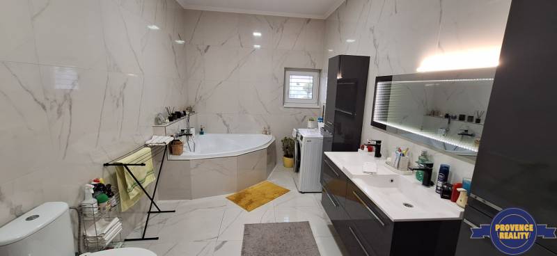 Kúpeľňa v rodinnom dome so vstavanou vaňou, umývadlom a práčkou, obložená svetlými kachličkami.